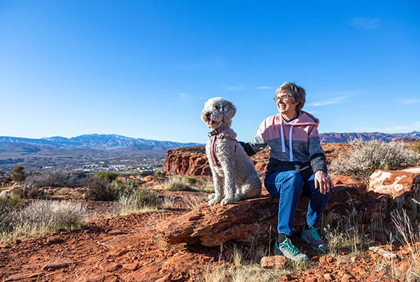A senior woman and a dog sitting on a desert outcrop in the sun